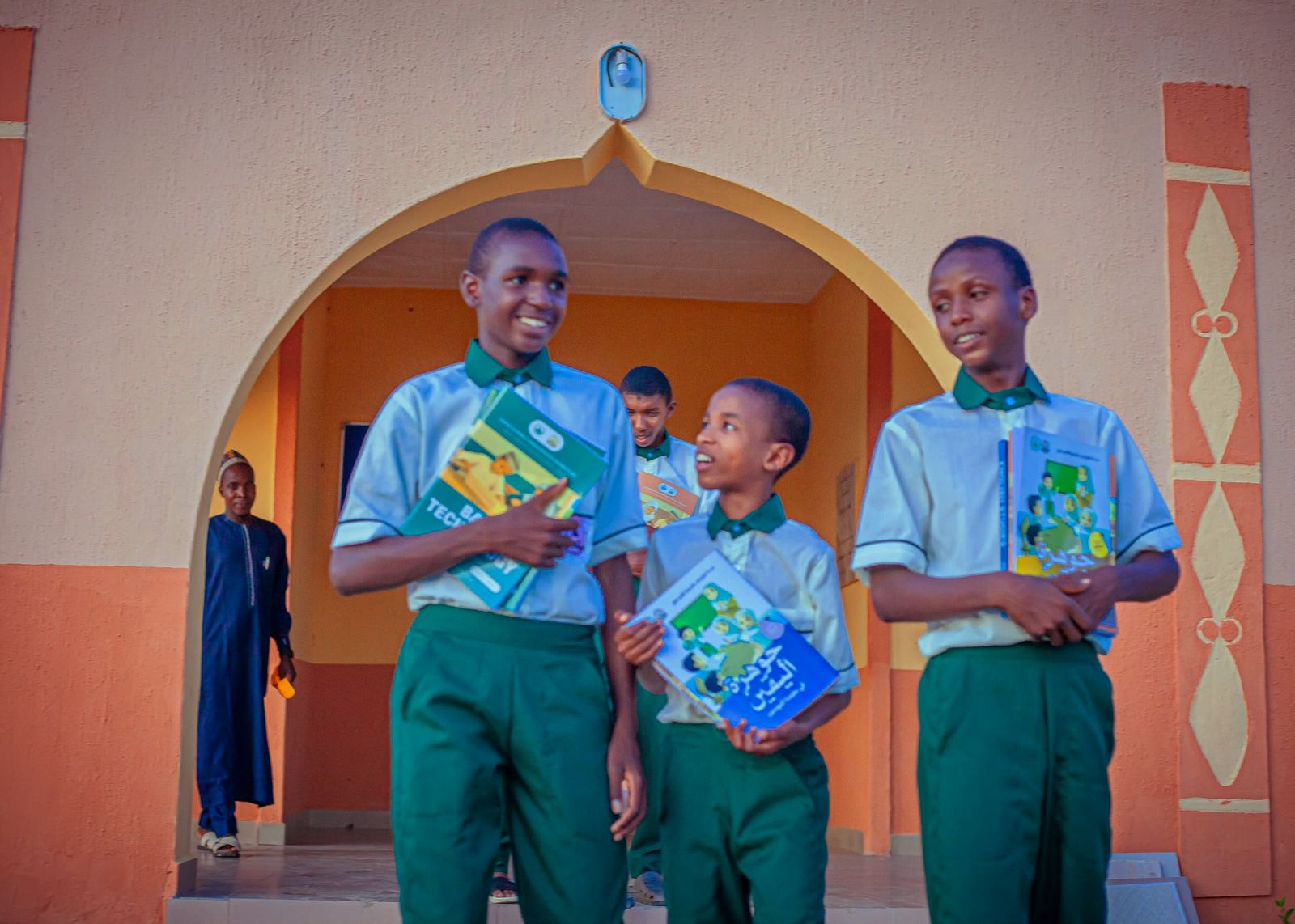 Three STTMSK pupils in their new uniforms walking out of the school's arch with their books